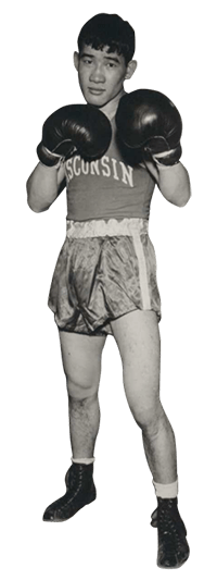 Akio Konoshima,a Japanese-American student athlete, stands with fists up in boxing gloves wearing the Wisconsin team boxing uniform.