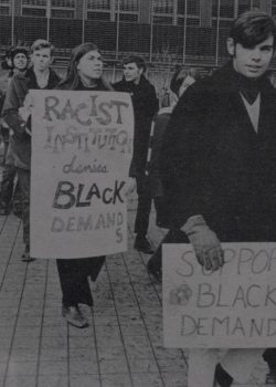 Student protesters marching with signs that read “racist institution denies Black demands” and “support Black demands” during the 1969 Black Student Strike.