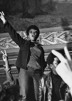Student holding up a Black power fist in front of a crowd at the Wisconsin state capitol building.