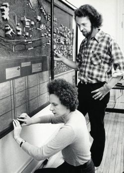 A student crouches in front of a large 3-D map reading the Braille text provided. A man stands behind her, observing.