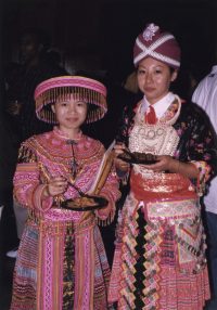 Two Hmong American Student Association members in full regalia enjoying food at an annual event.