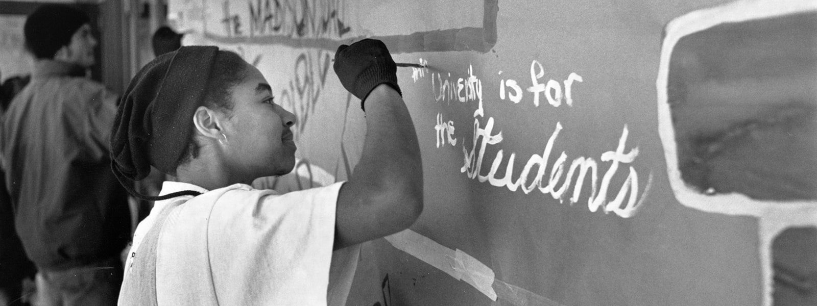 A student paints a message on a wall reading “the university is for the students”.